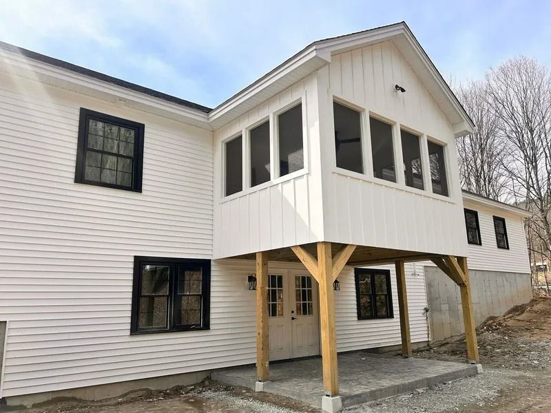 White house with a raised enclosed porch supported by wooden posts and a gravel driveway beneath it