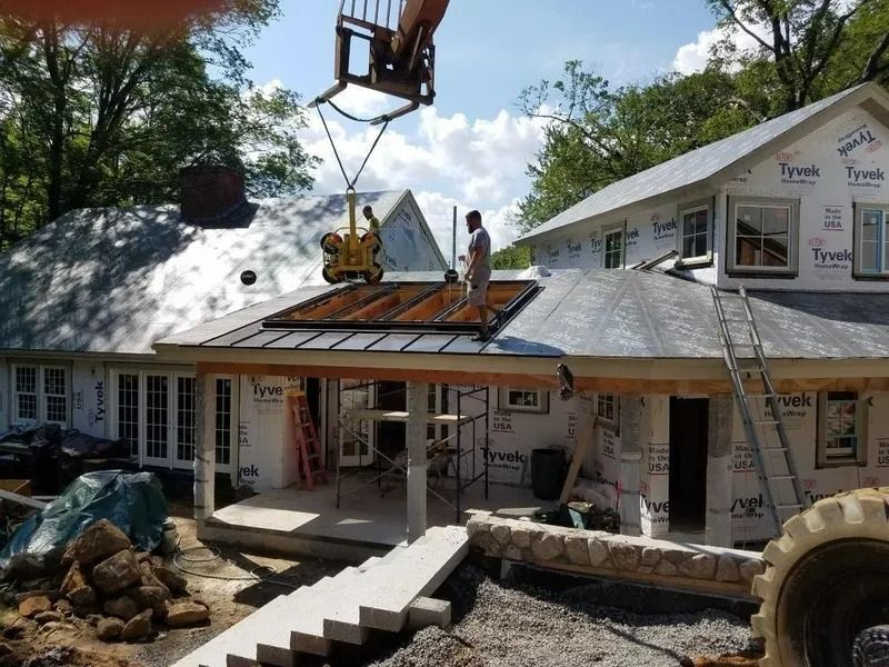 House under construction with workers on the roof and a crane lifting materials.