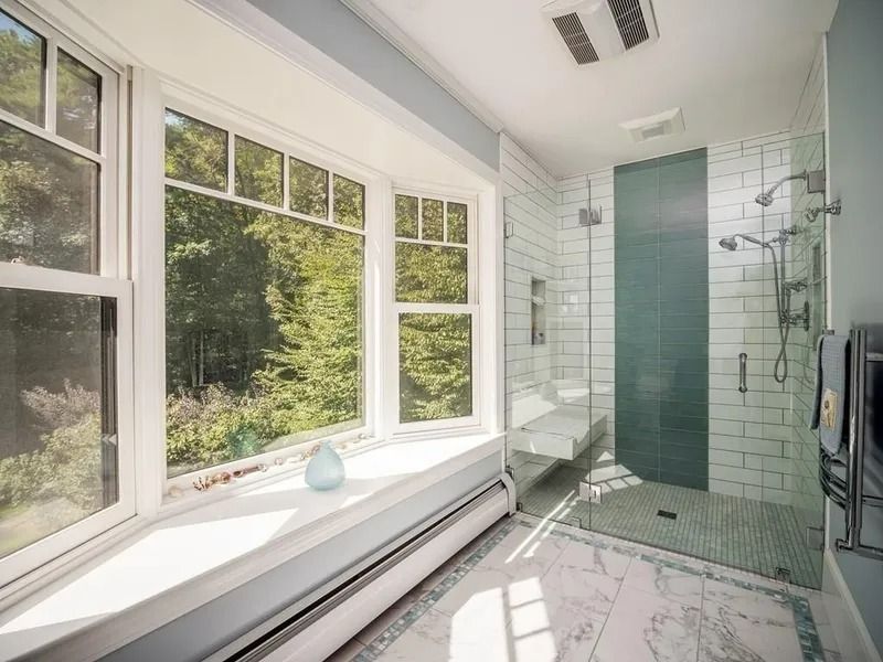 Bright modern bathroom with large windows, tiled shower, and natural light overlooking greenery