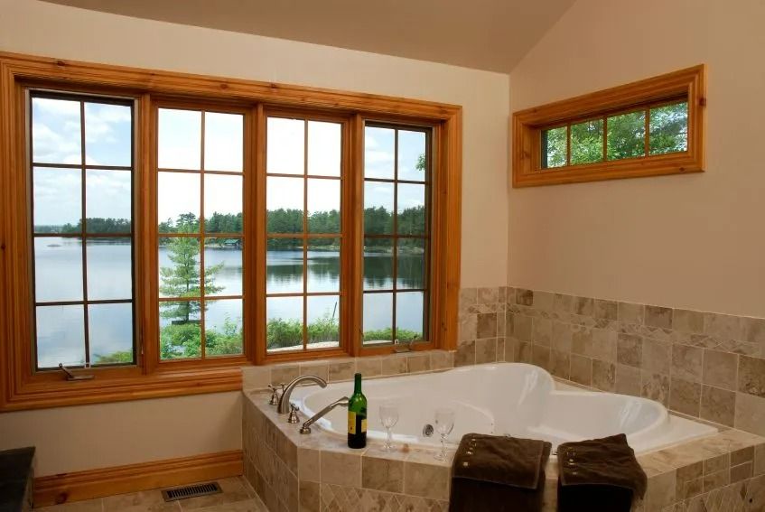 Bathroom with a large soaking tub, wood-framed windows, and a lake view