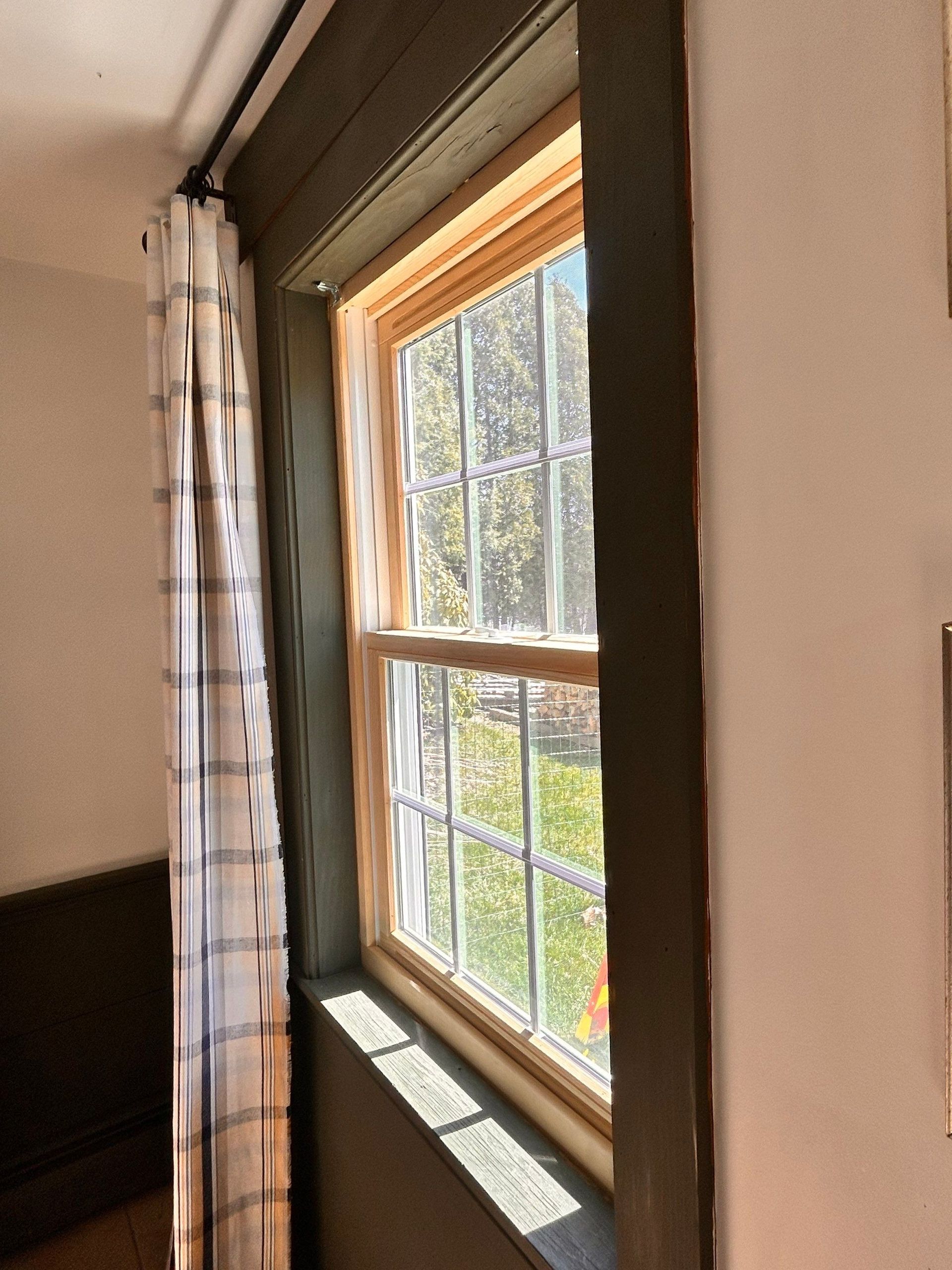 Sunlit window with white curtains and a view of green trees outside