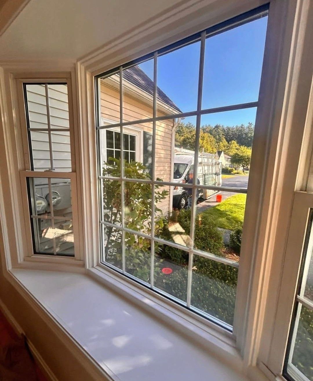 Window seat view of a sunny suburban yard and neighboring brick house through white-framed panes