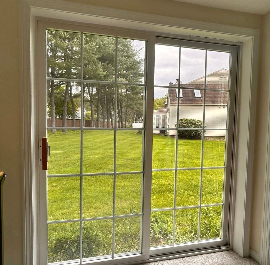 Sliding glass door with white grid panes looking out onto a green backyard and neighboring houses