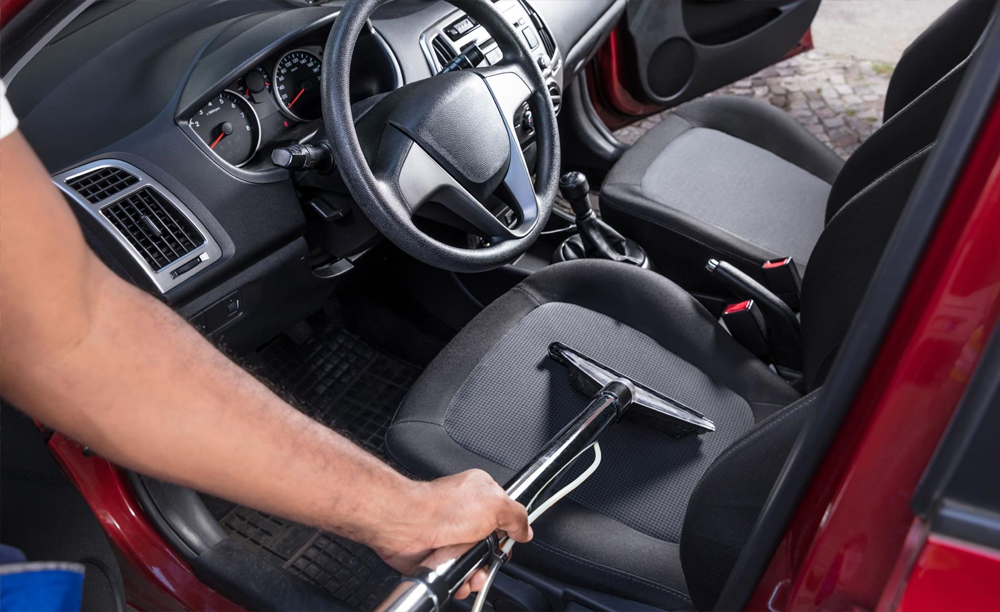 Person vacuuming car seat in red car.