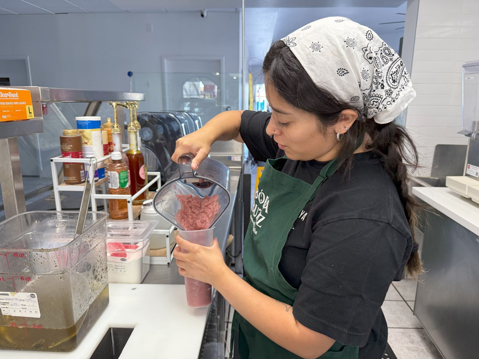Woman with a bandana pours a blended smoothie into a cup behind a counter in a cafe
