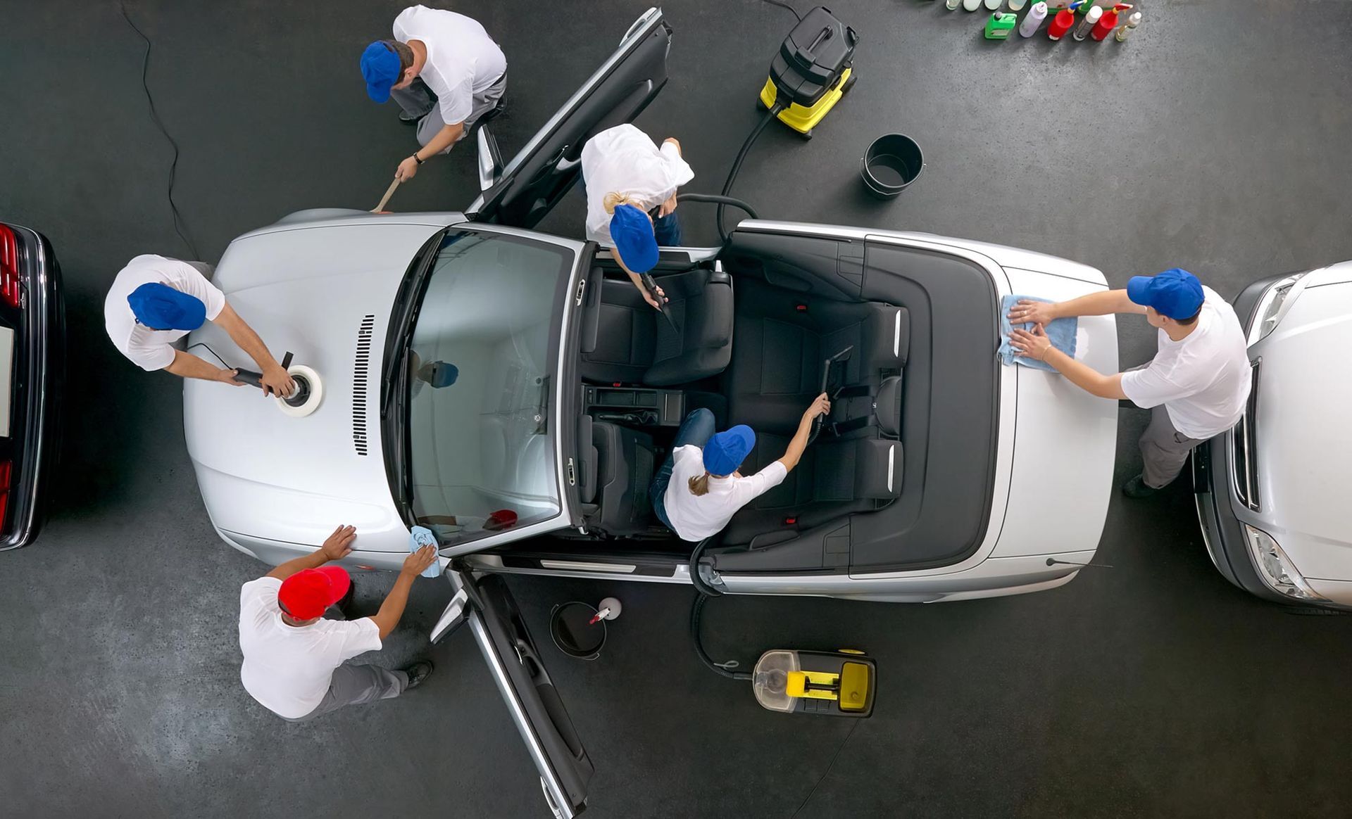 A group of people are cleaning a car in a garage