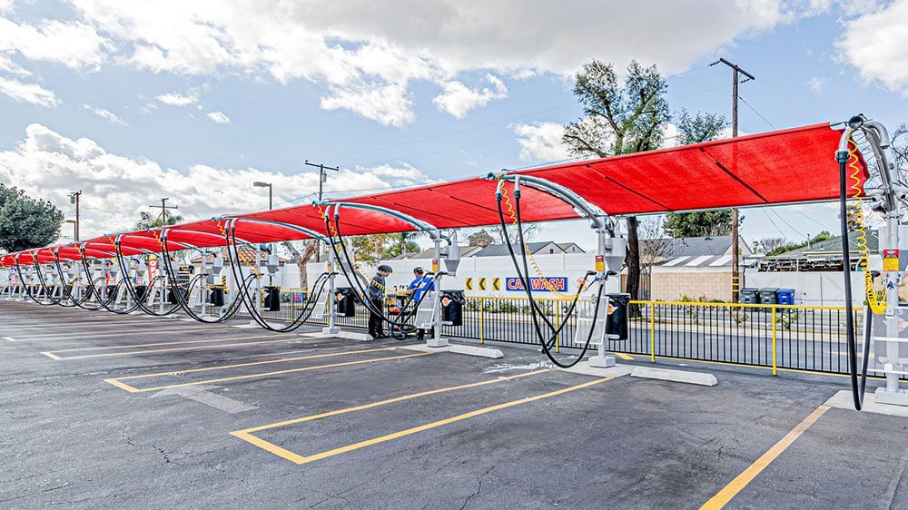 A row of cars are being washed at a car wash under a red canopy.