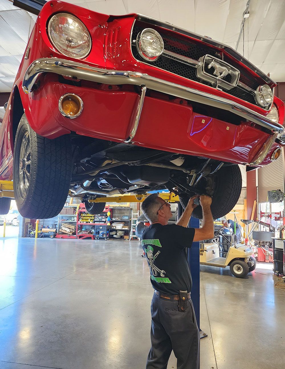 A man is working on a red mustang in a garage