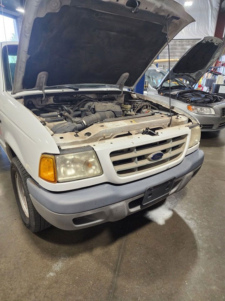 A white ford ranger with the hood up in a garage.