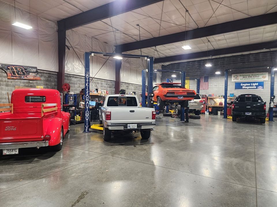 A red truck is parked in a garage next to a white truck.