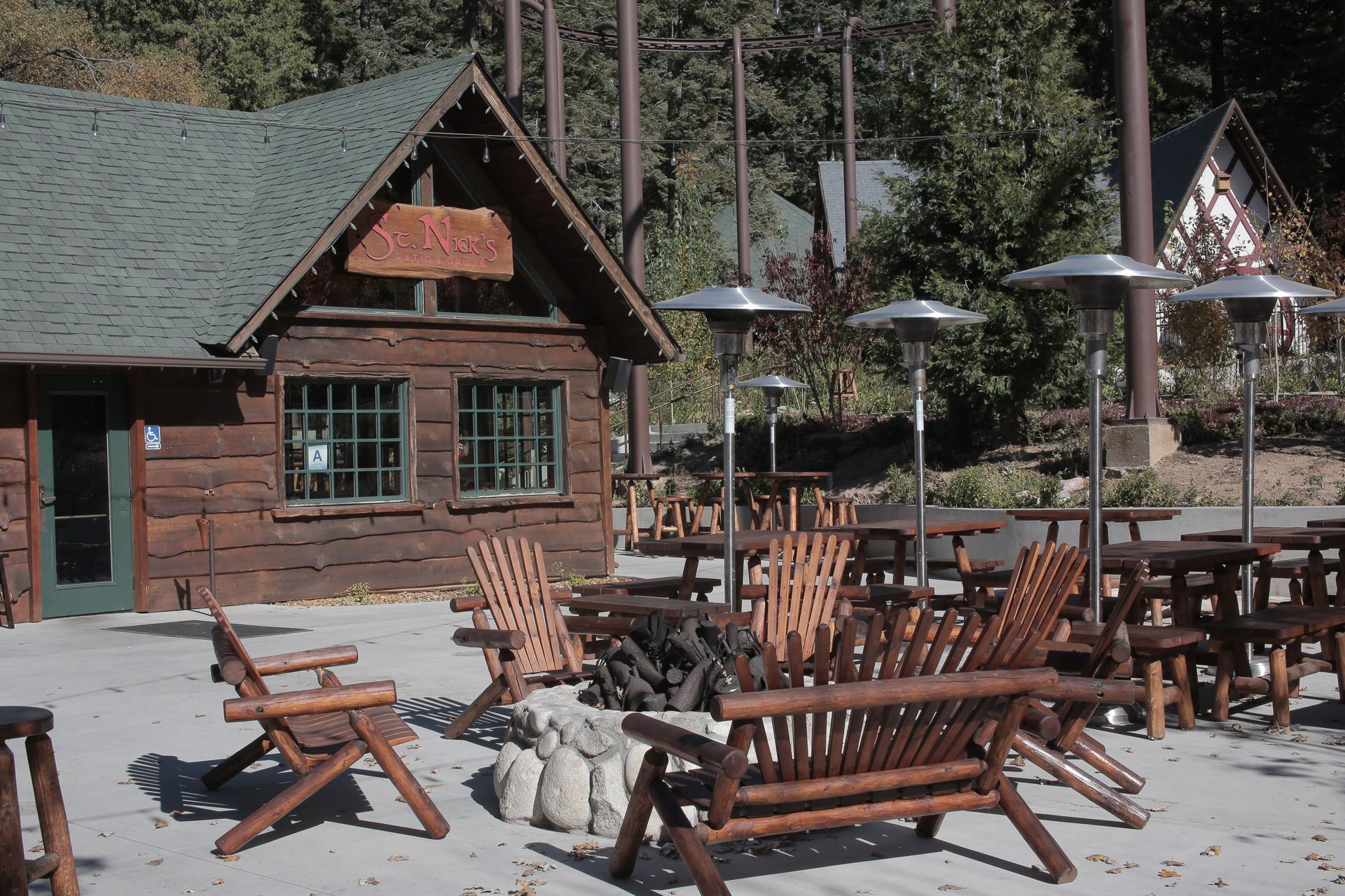 Rustic cabin with outdoor seating area; brown log building, wooden chairs, patio heaters.