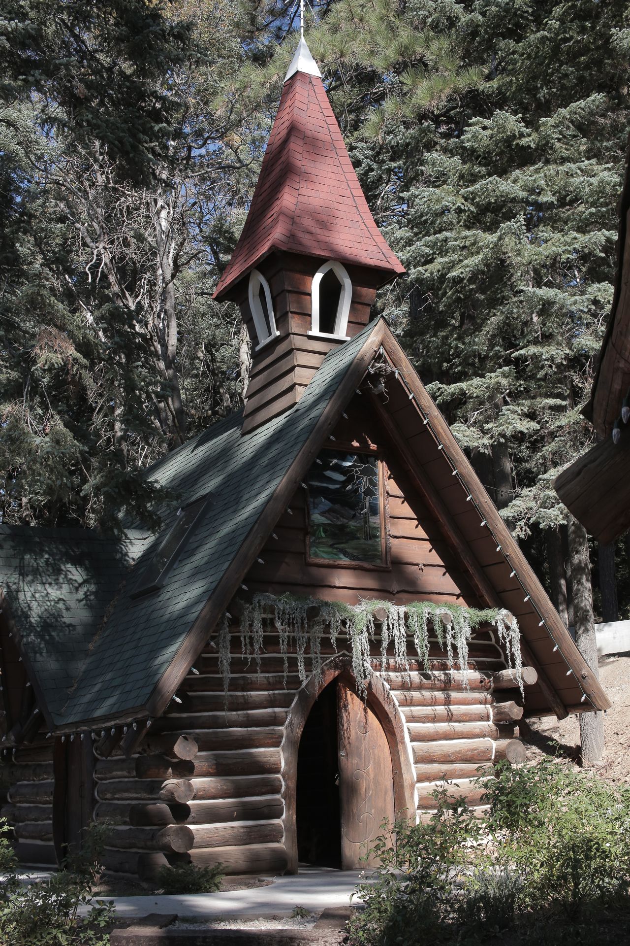 Wooden chapel with a red-roofed spire, in a forest setting.