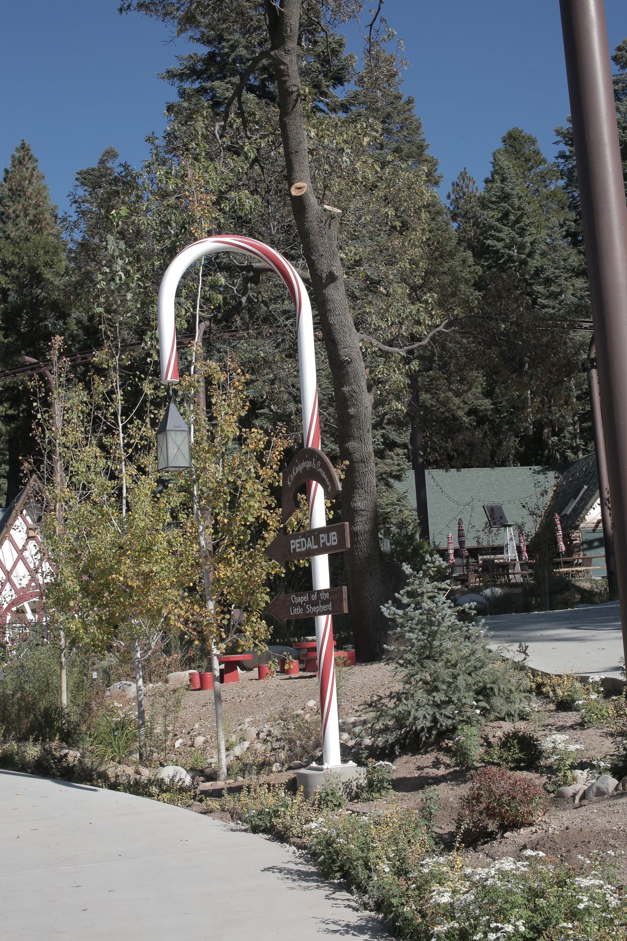 Candy cane shaped sign in a garden with trees and buildings in the background.