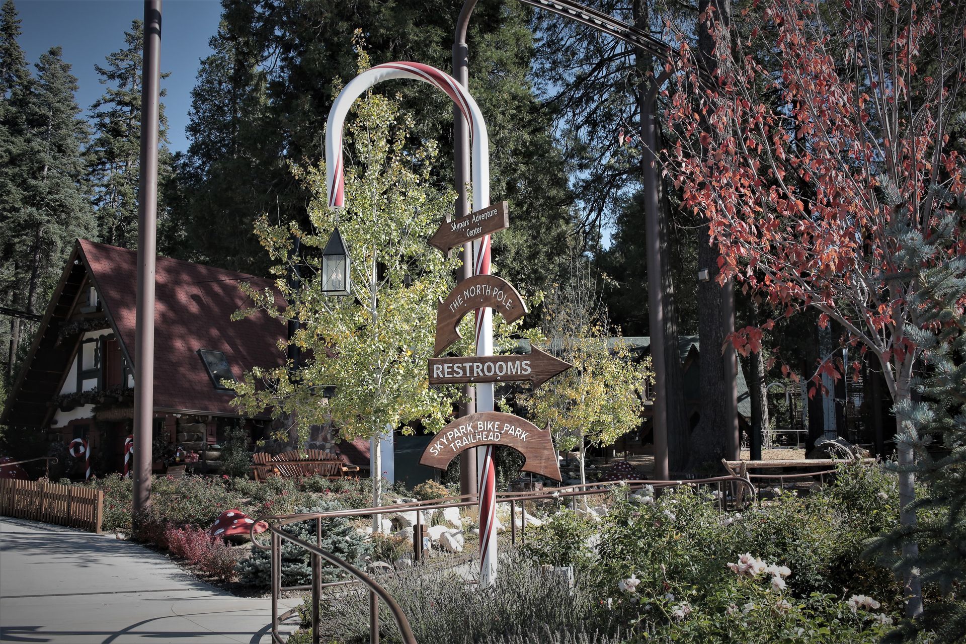 Signpost in front of a restaurant, pointing directions. Red and white arch, trees in background.
