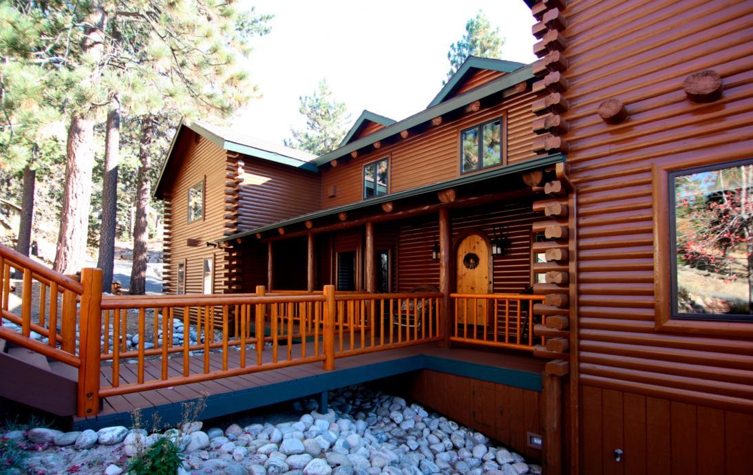 Wooden cabin with porch and bridge, brown wood, and a rocky ground.
