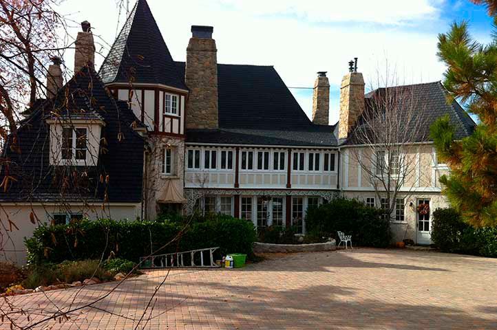Large house with a dark roof and multiple chimneys, light-colored walls, and a circular driveway.