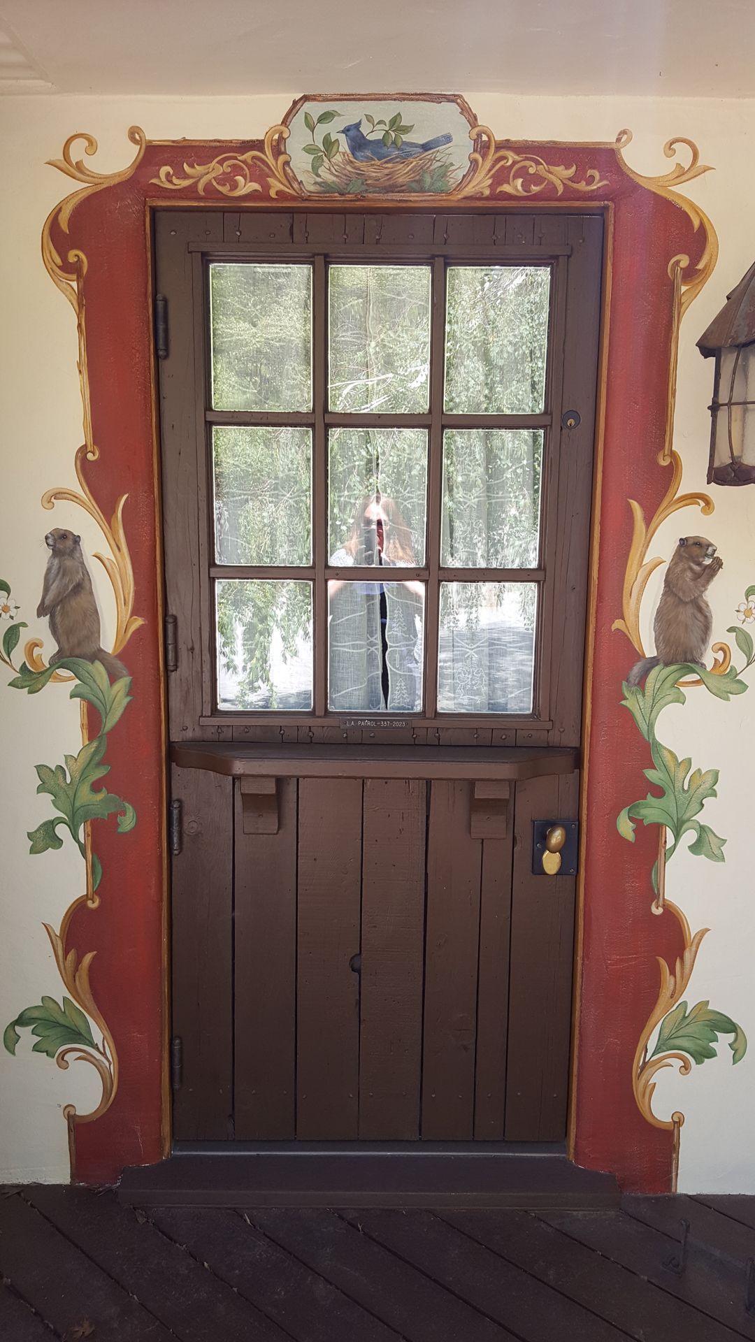 Brown dutch door with a window, set in a painted red and green frame with squirrel figures.