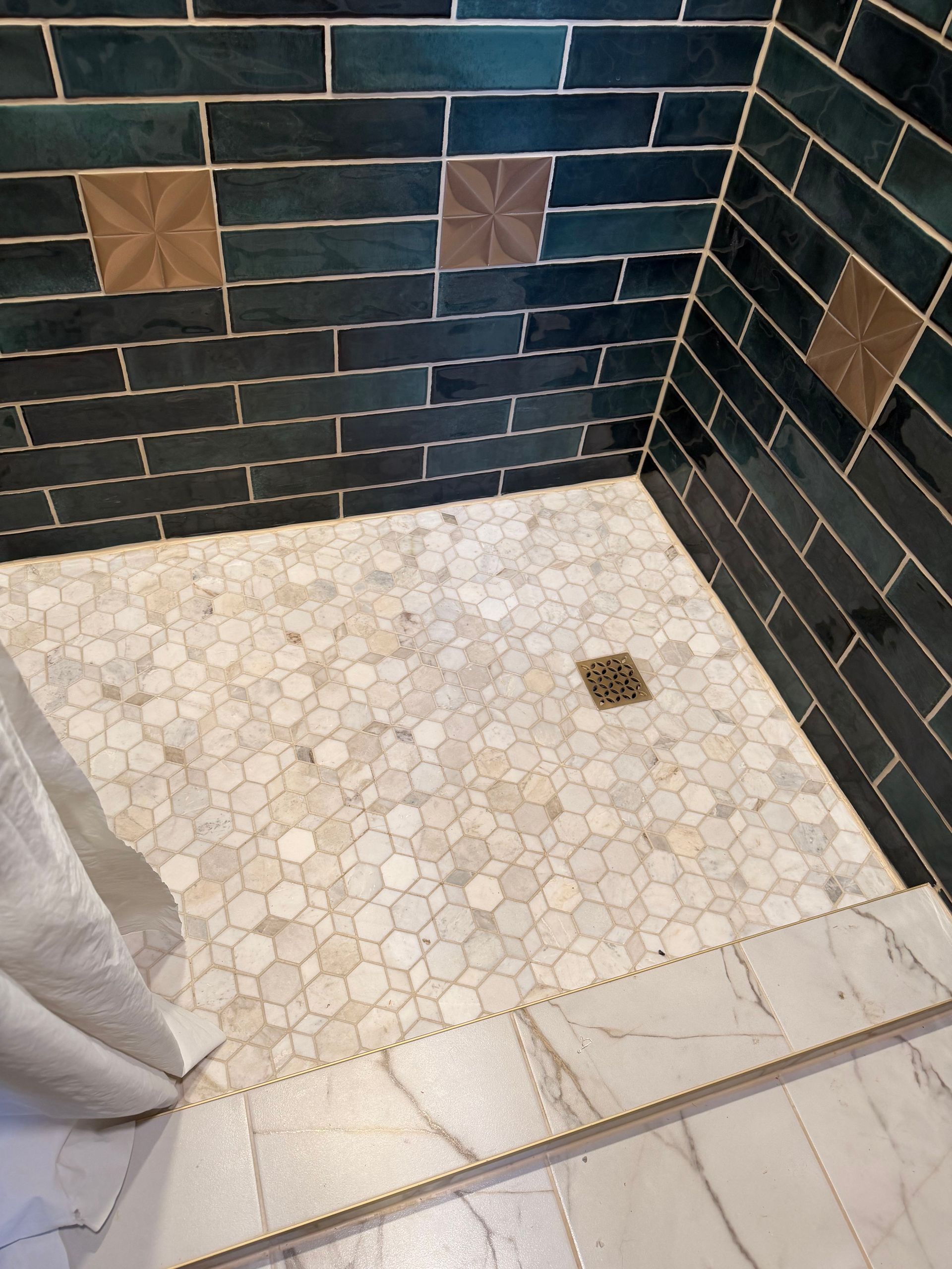 Tiled shower corner with dark wall tiles, mosaic floor, and a small drain.