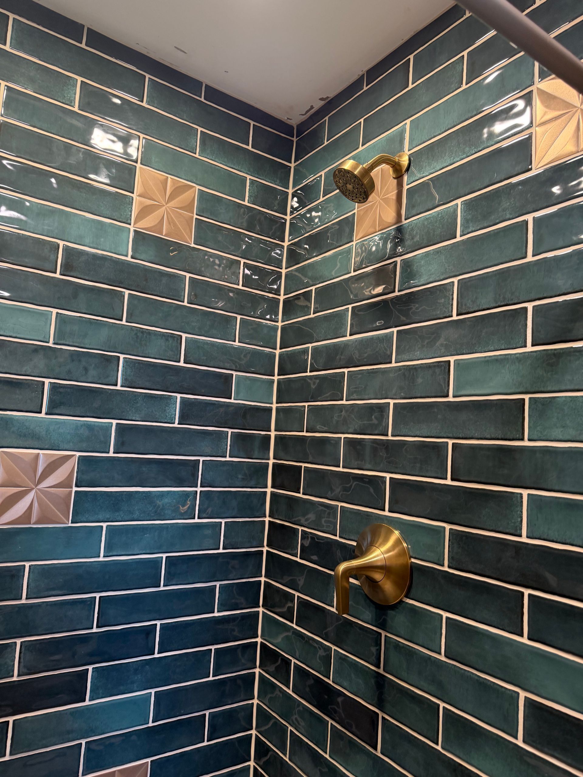 Teal subway-tile shower corner with brass fixtures and small square accent tiles