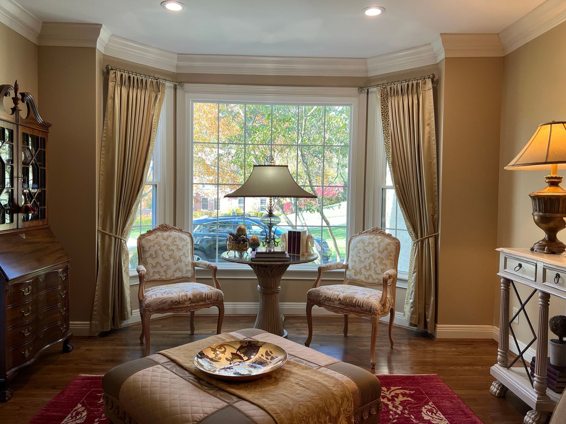 Elegant living room with bay window, two armchairs, ottoman, and table lamp on a side table