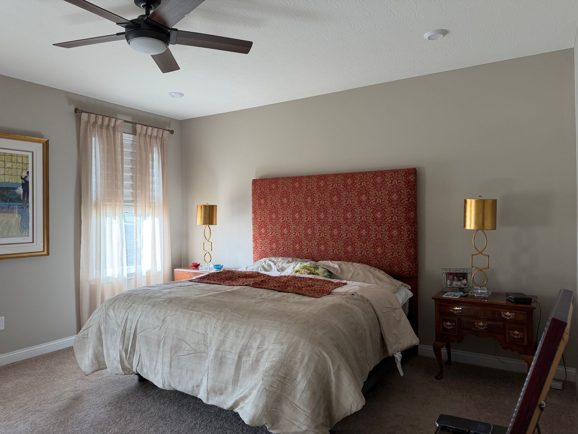 Bedroom with a bed, red upholstered headboard, bedside tables, and a ceiling fan near a window.