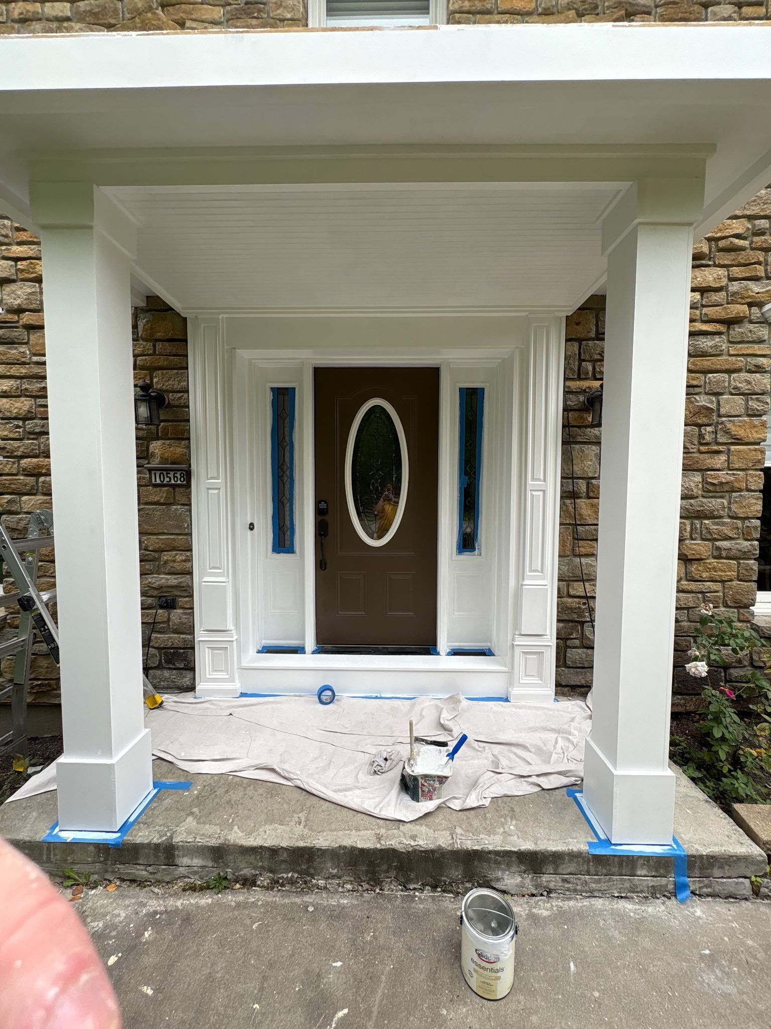 Front porch entry under construction with white trim, stone columns, and protective covering on the floor