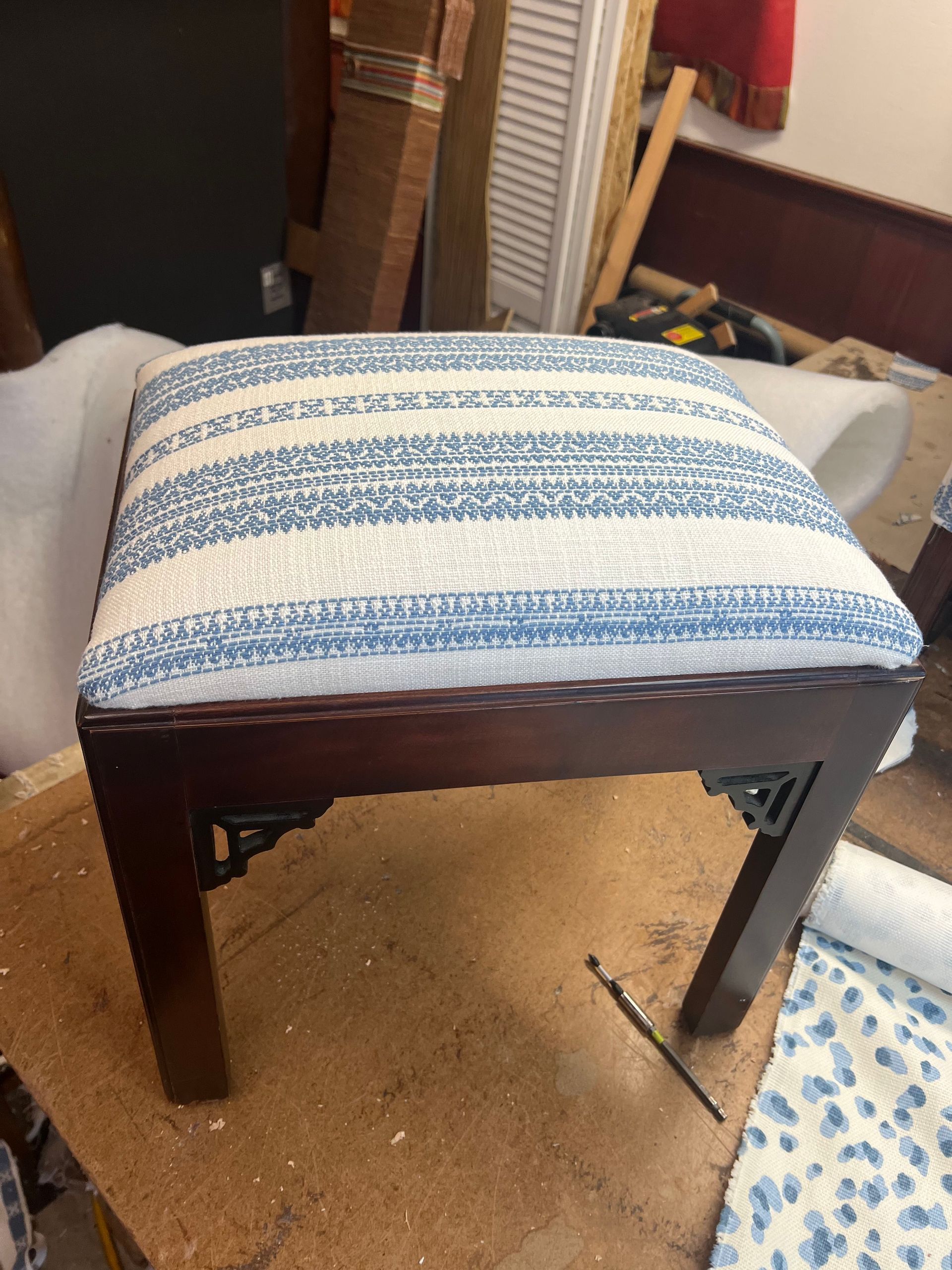 Blue-and-white striped upholstered stool with dark wooden legs on a carpeted floor.