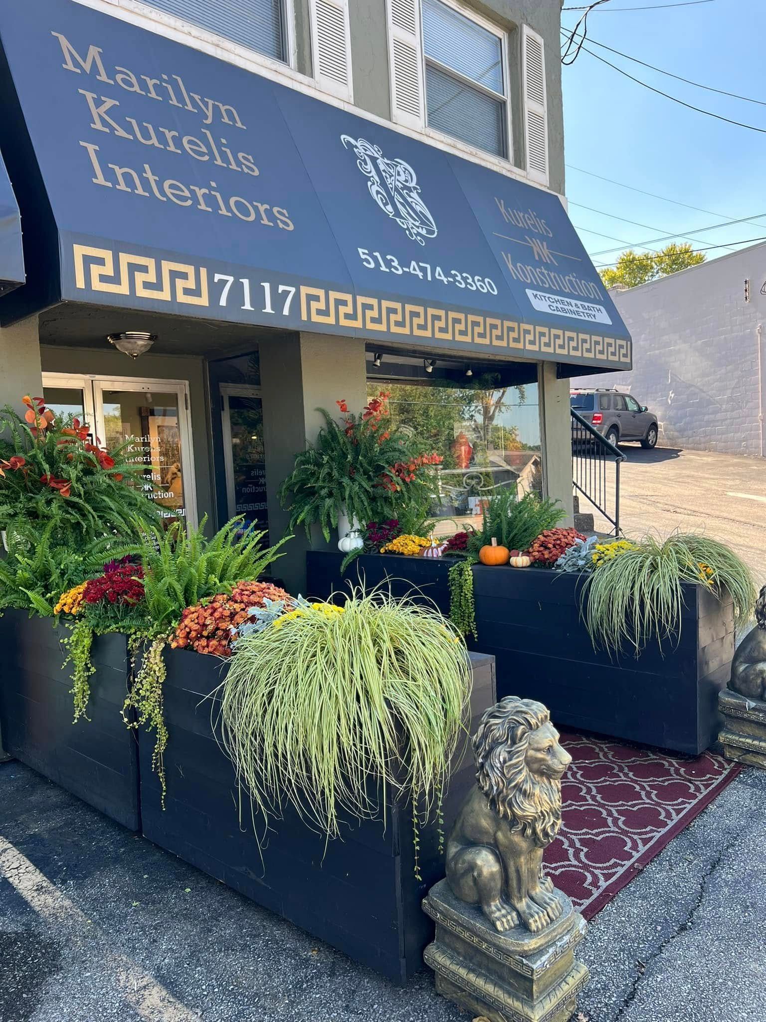 Martinis Kafe & Interiors storefront with blue awning, flower boxes, and a small statue by the entrance