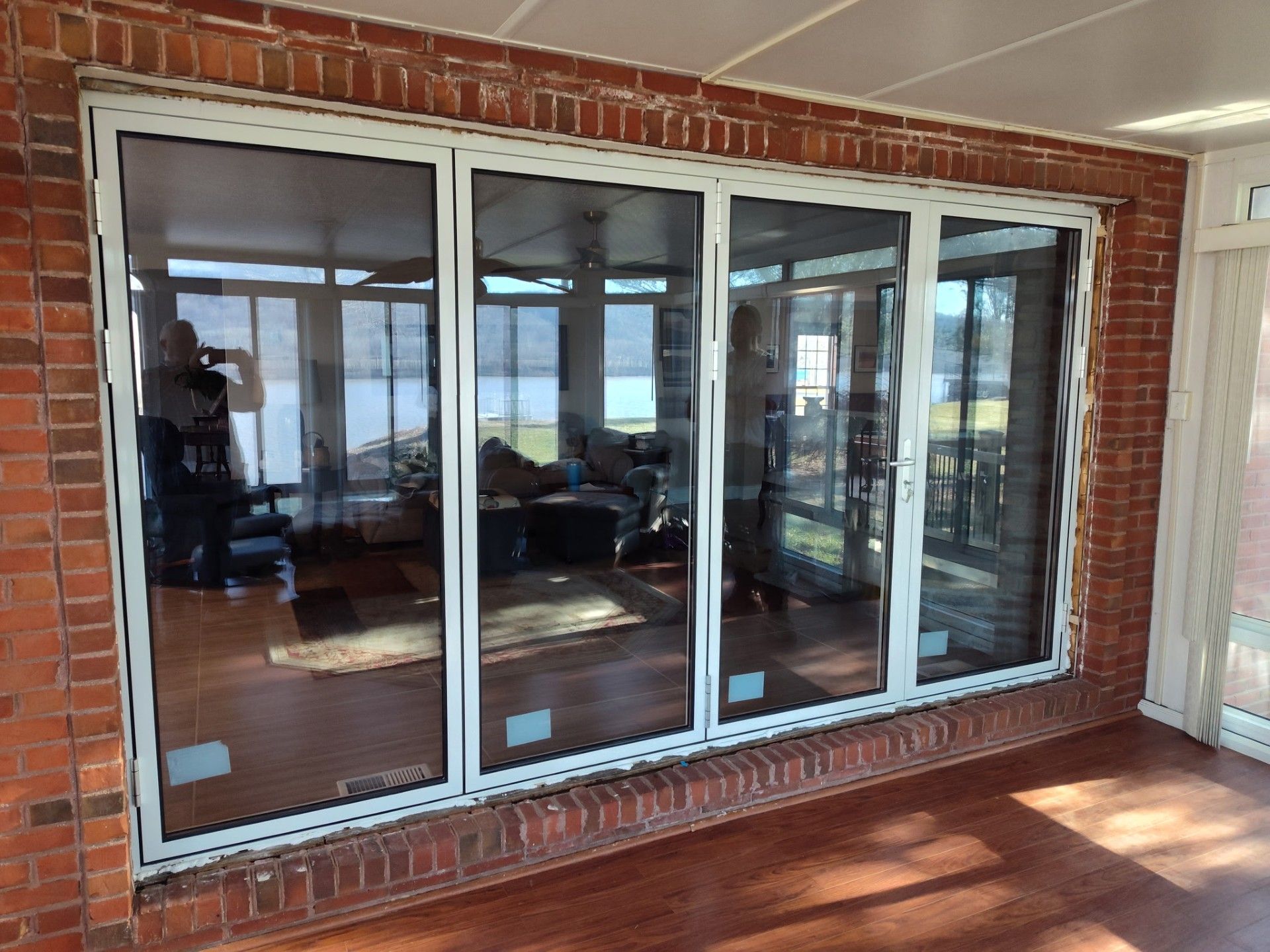 Sliding glass doors with white trim set into a brick wall, reflecting a patio and interior room.