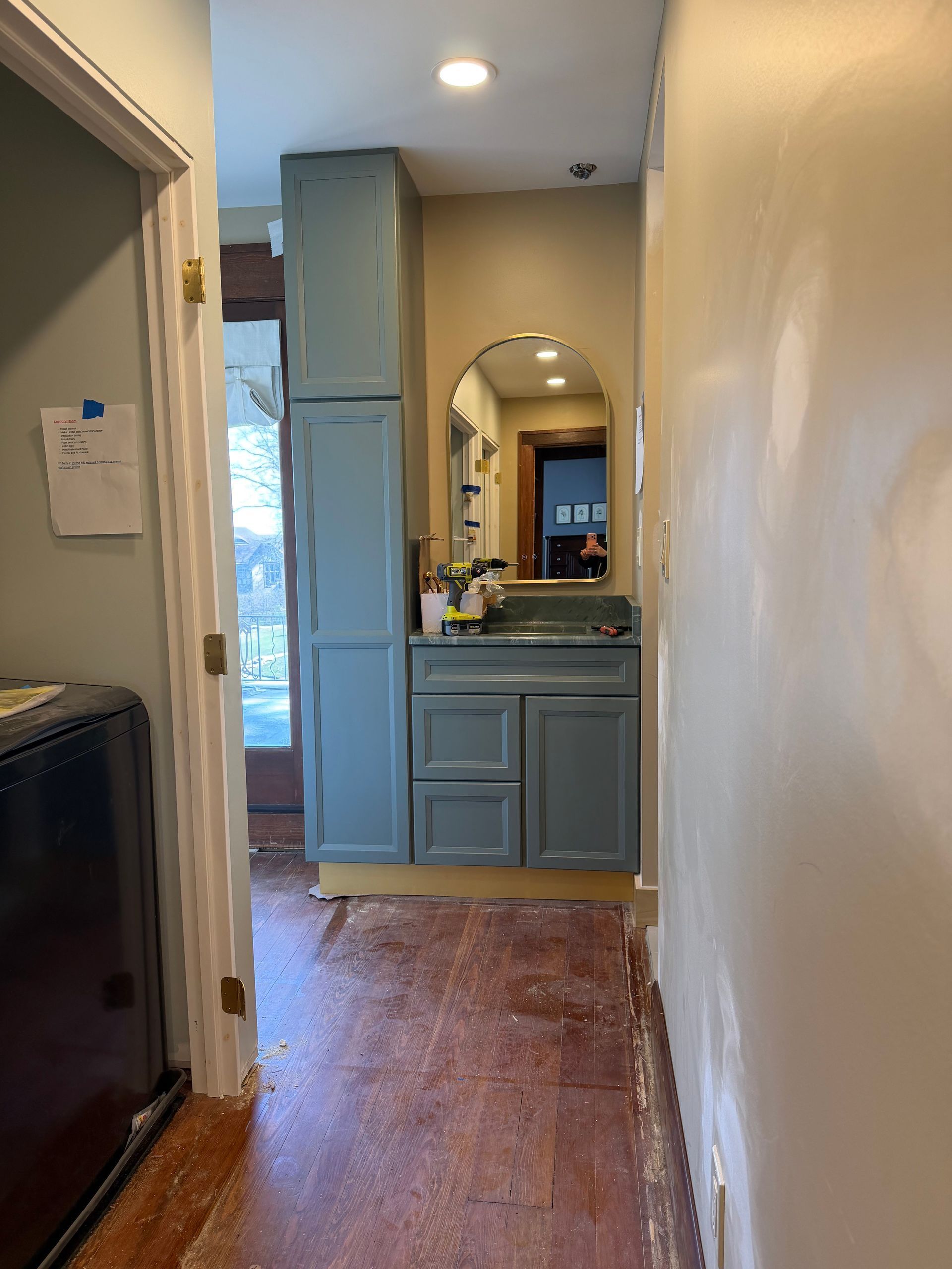 Narrow hallway with wood floor leading to a bathroom vanity and mirror, lit by ceiling lights.