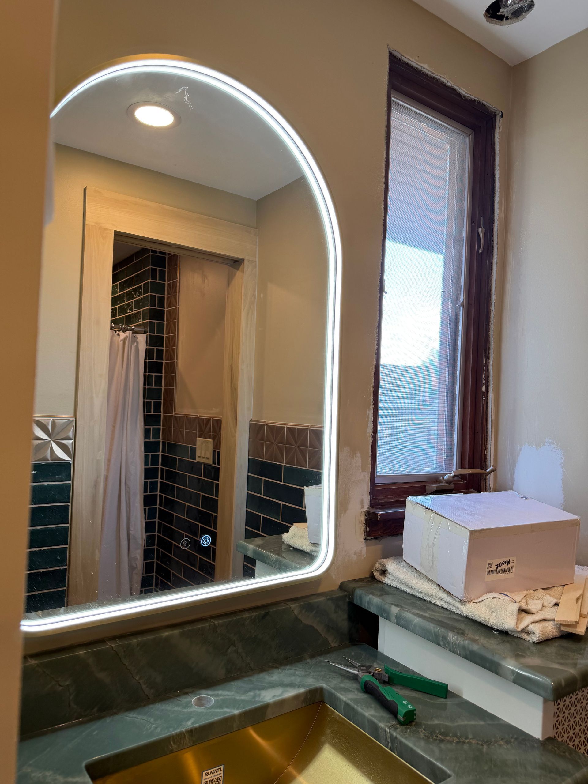 Bathroom sink and illuminated mirror beside a window with blinds and a soap dispenser.