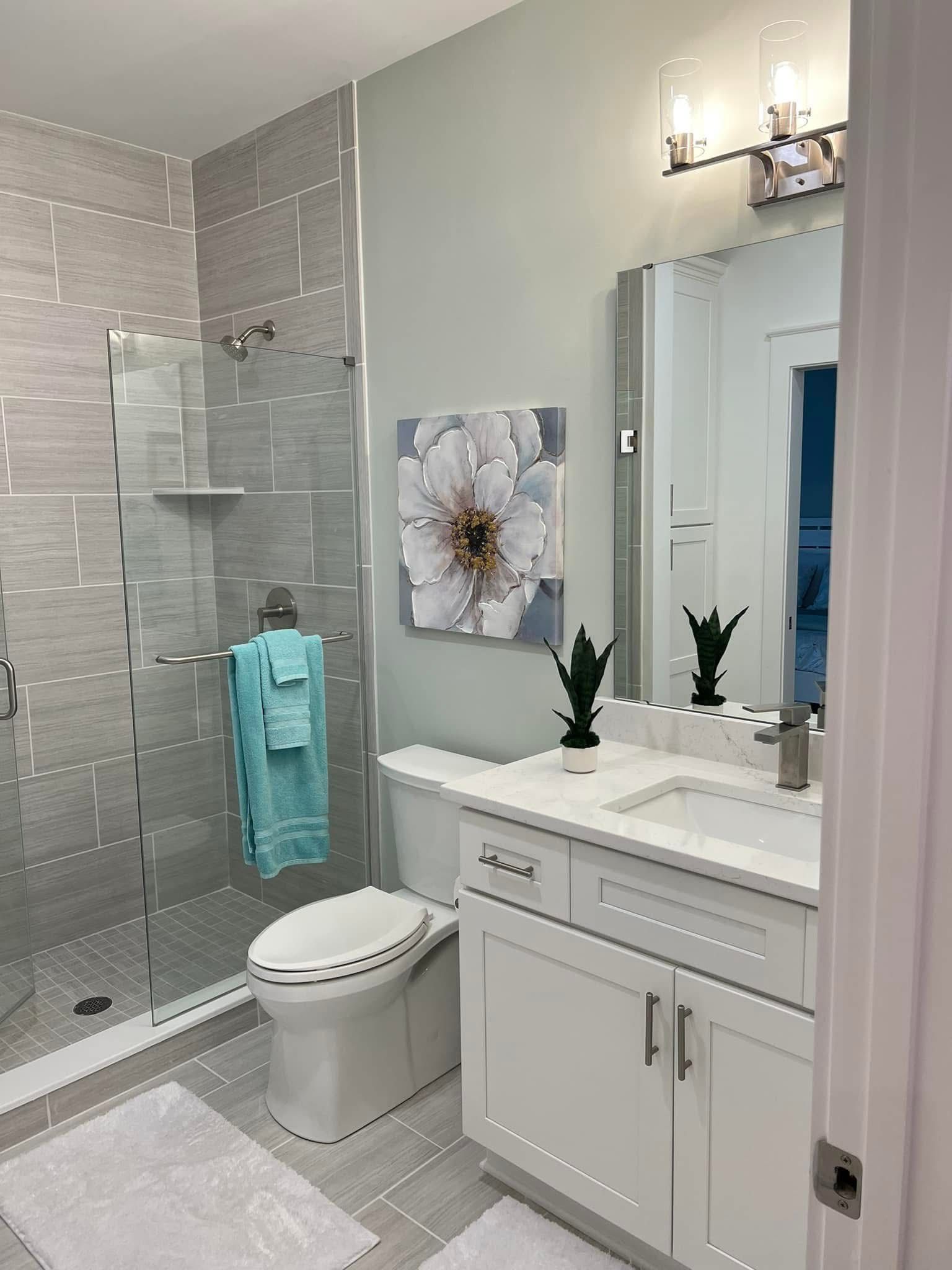 Bright modern bathroom with glass shower, white vanity, mirror, and toilet with turquoise towel.