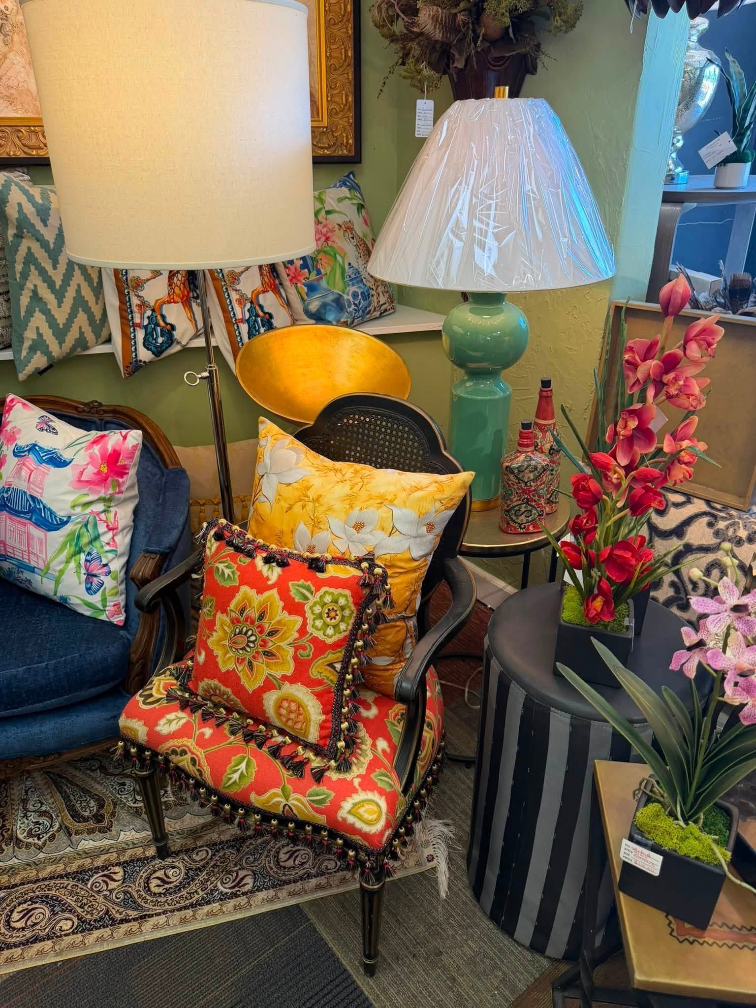 Colorful upholstered chairs, patterned pillows, and lamps in a cozy, eclectic living room with flowers.