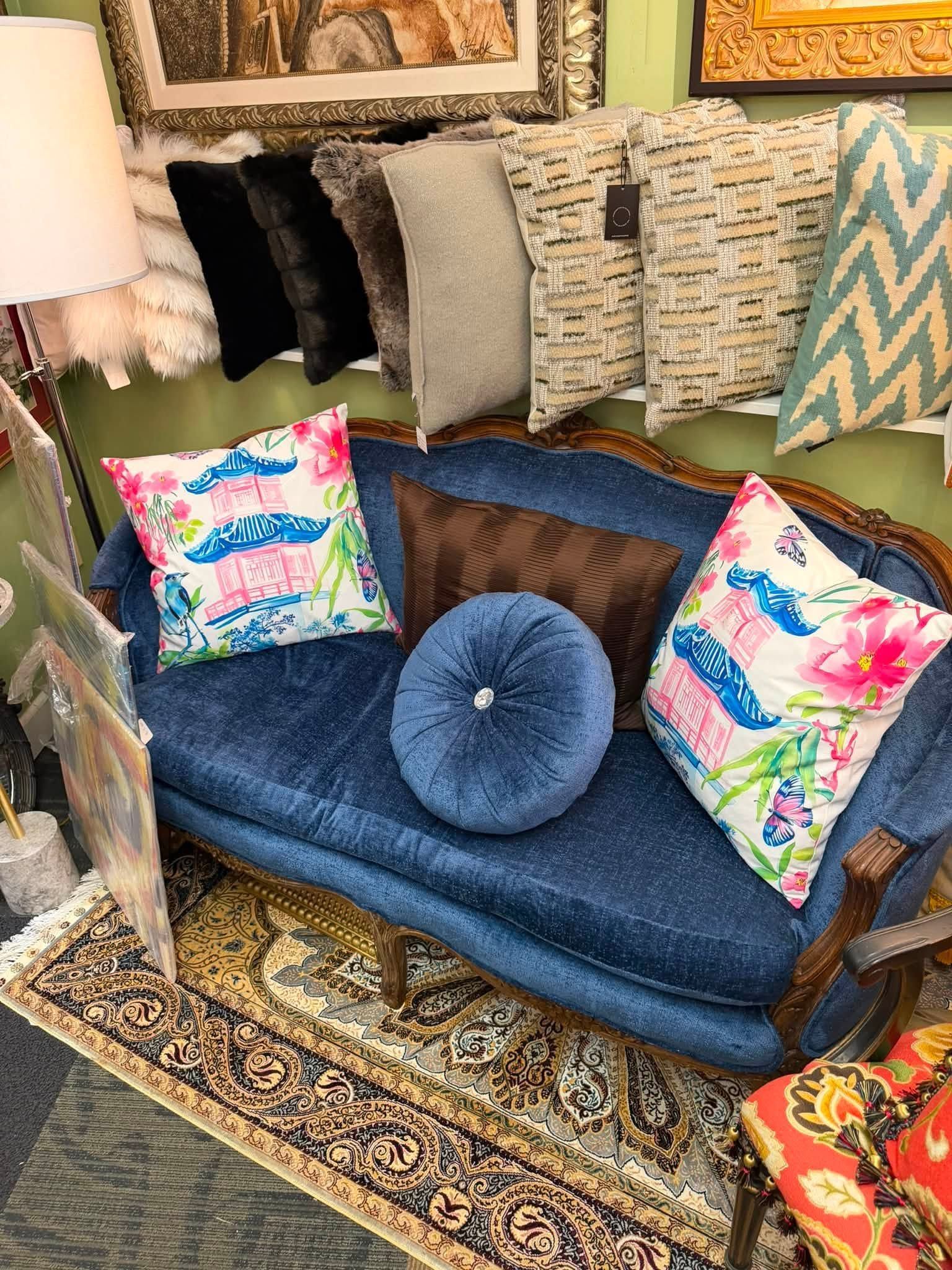 Blue loveseat with floral pillows and round cushion in a cozy, patterned living room corner