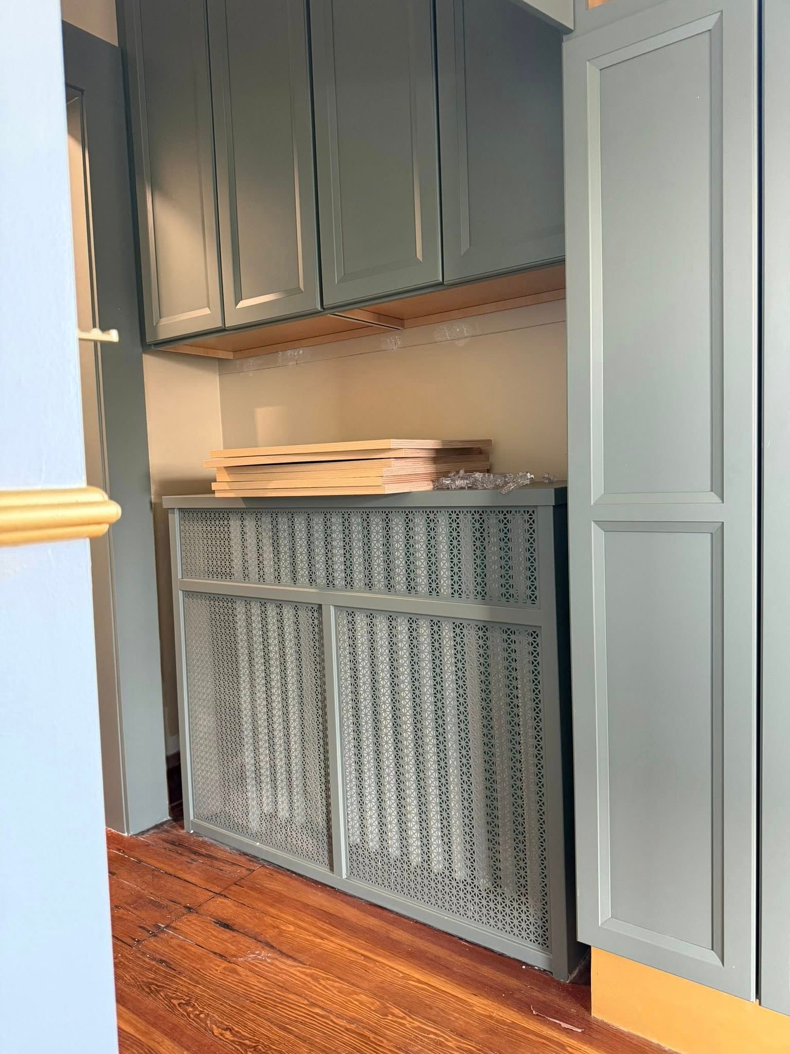 Gray cabinet in a hallway alcove with woven doors, upper storage cabinets, and wooden trays on top
