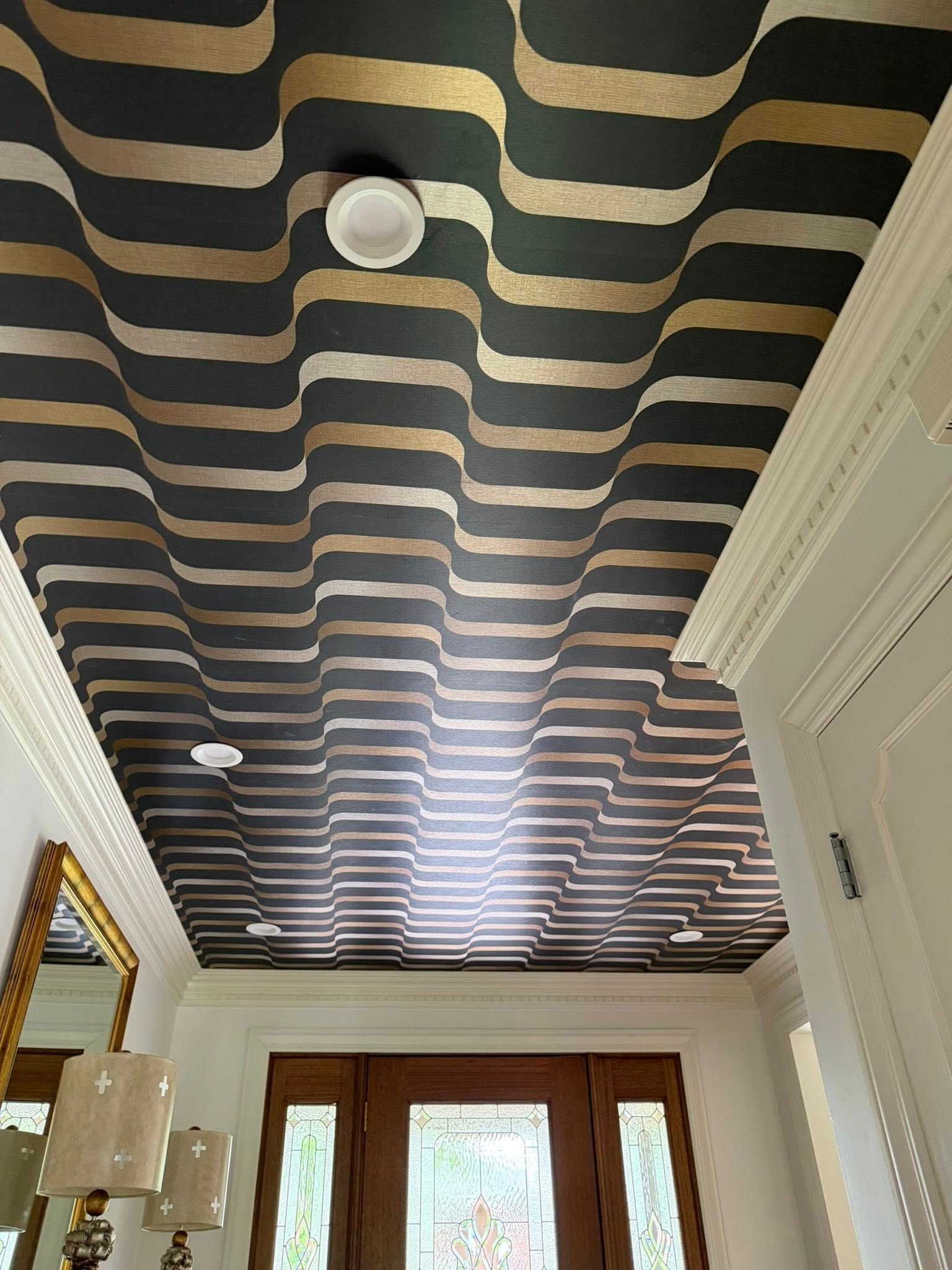 Modern hallway with black-and-beige striped ceiling, white walls, and bright French doors at the end