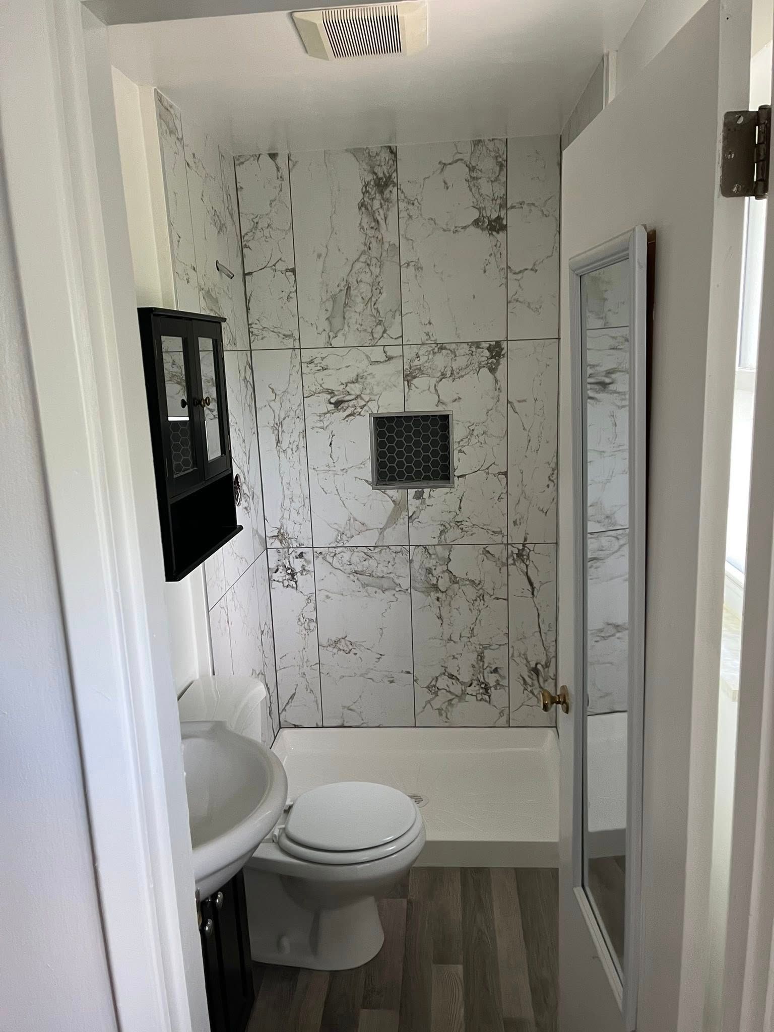 Small bathroom with toilet, sink, shower, and marble-patterned wall tile.