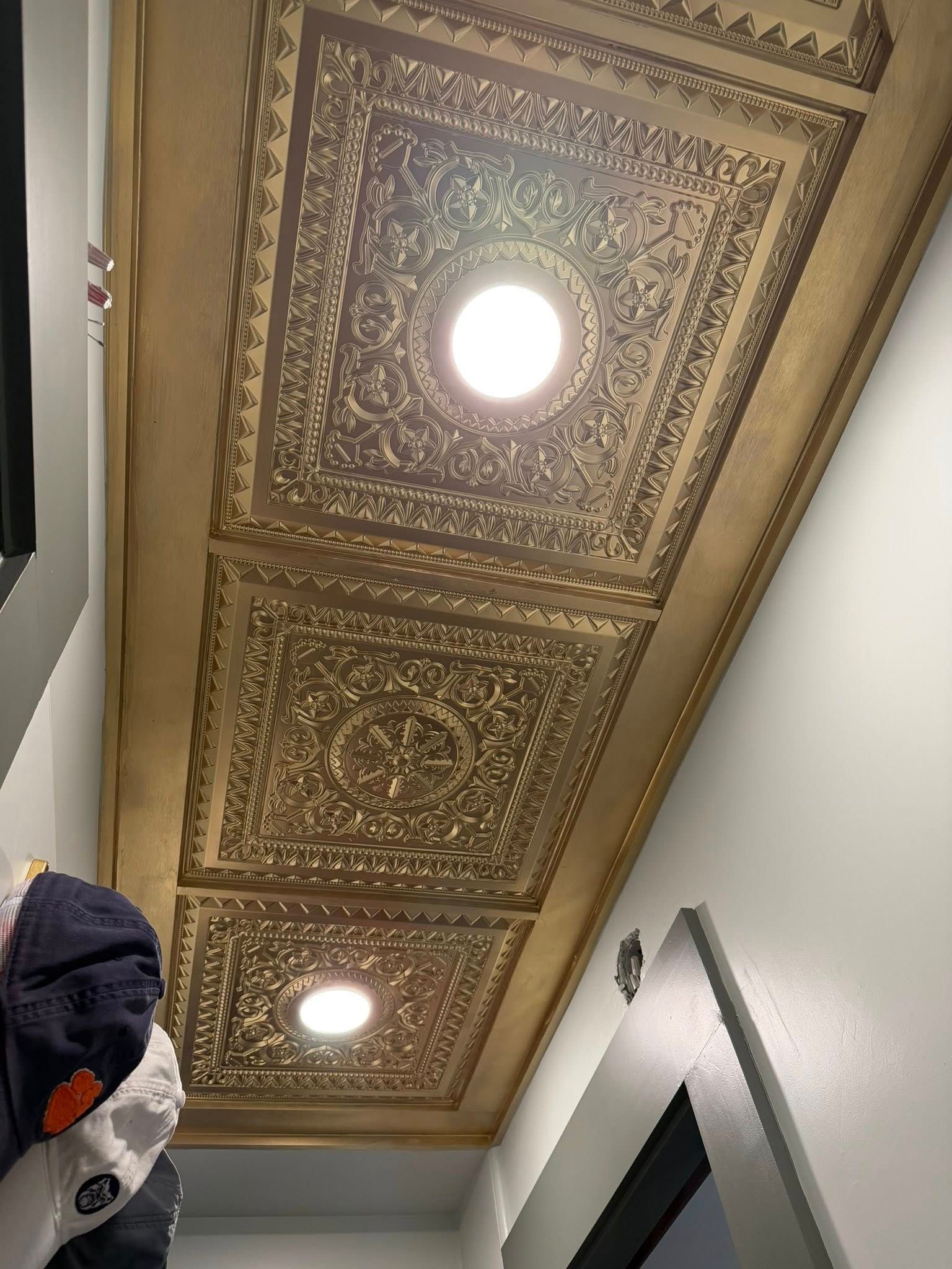 Ornate gold ceiling with recessed lights above a hallway or corridor