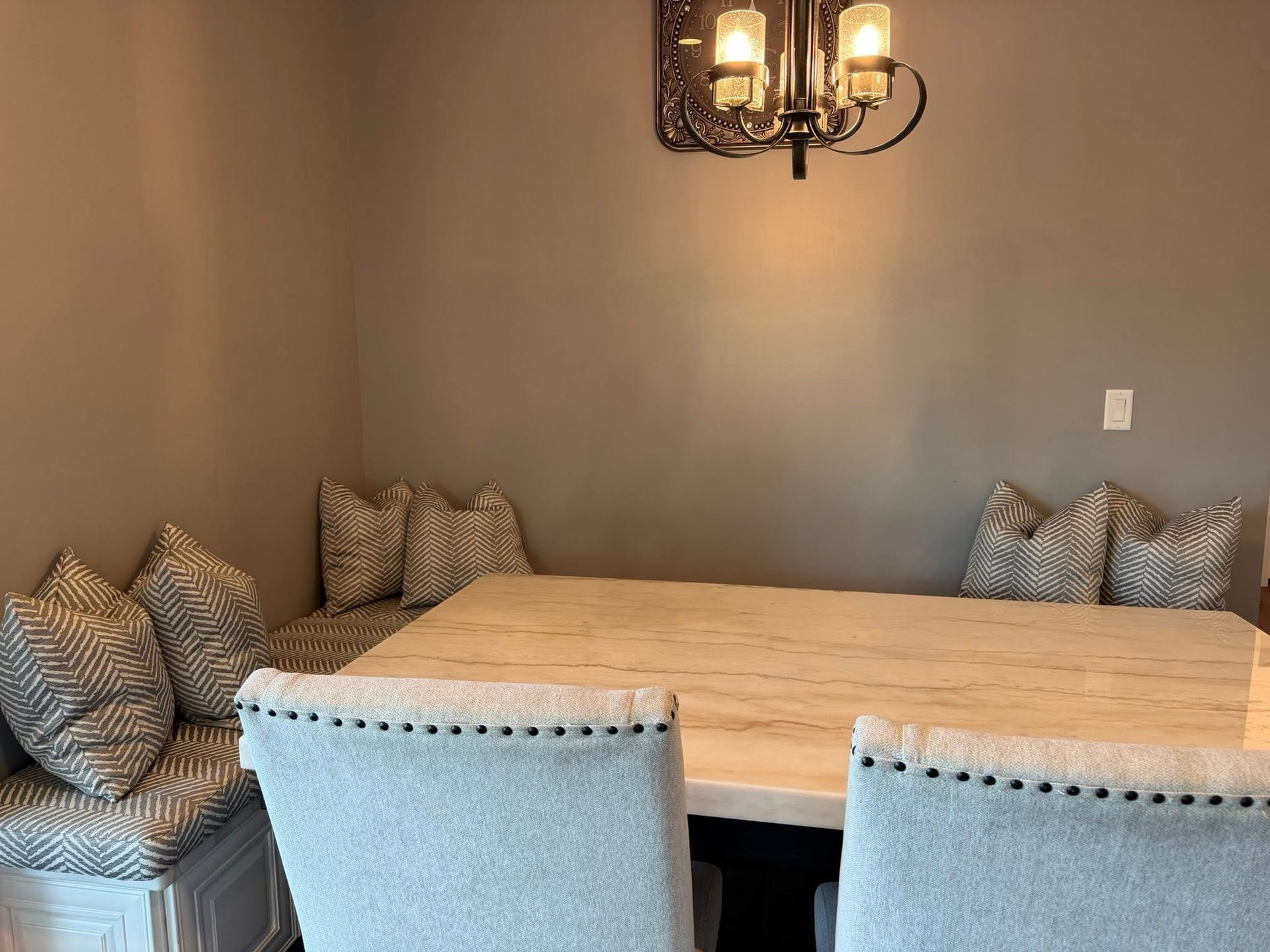 Dining nook with gray walls, wooden table, upholstered bench seating, and a hanging chandelier.