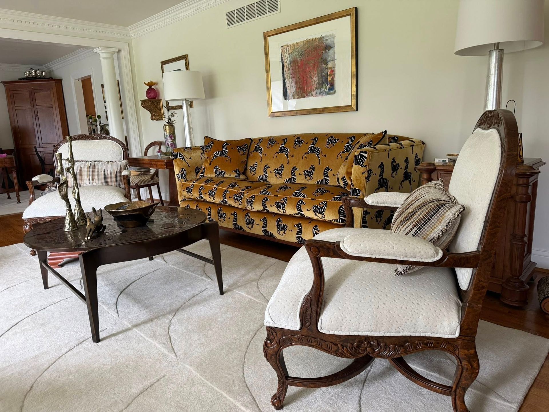 Elegant living room with patterned sofa, cream armchairs, glass coffee table, and framed wall art.