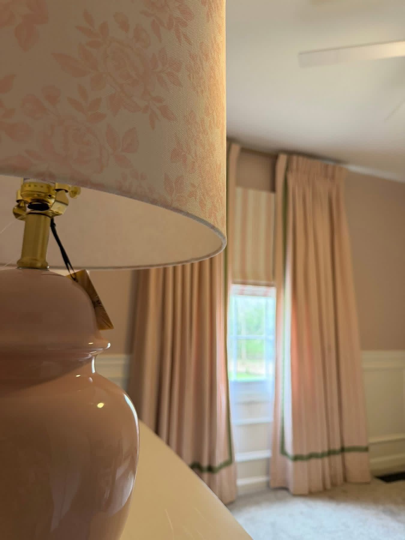 Beige lampshade and ceramic lamp in a bright room with beige curtains and a window
