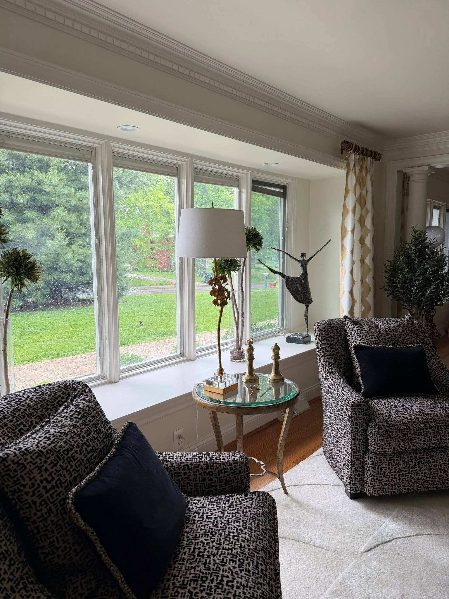 Bright living room with leopard-print chairs, glass coffee table, and large windows overlooking a green yard