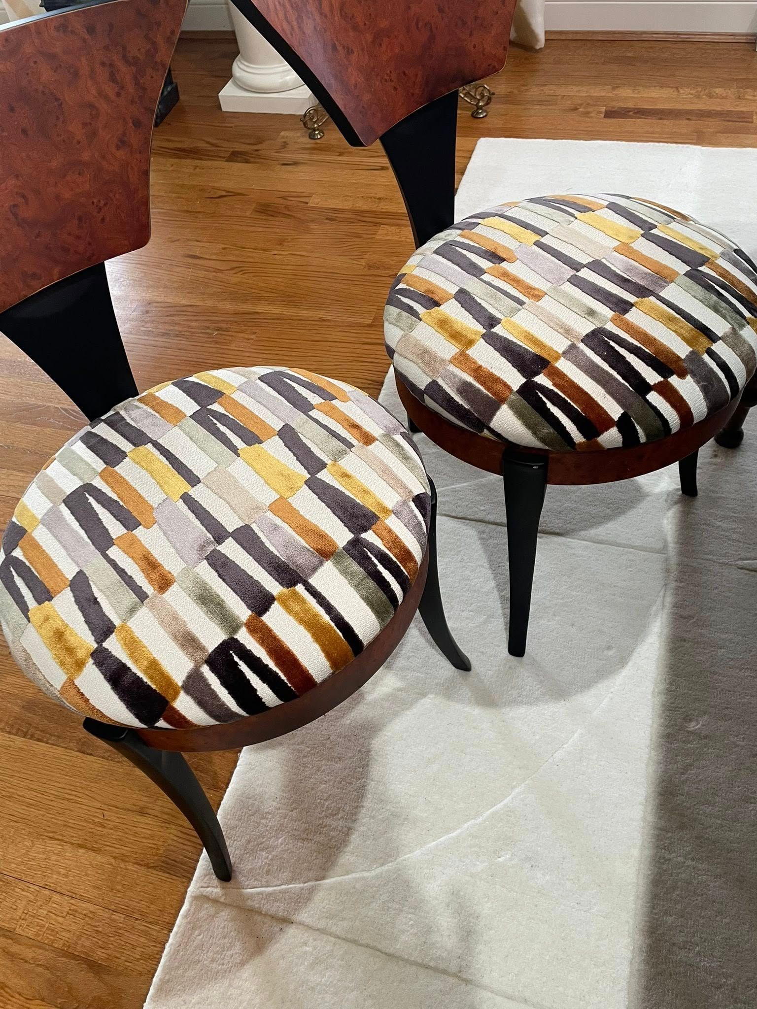 Two patterned upholstered dining chairs with black legs on a light rug over wood flooring.