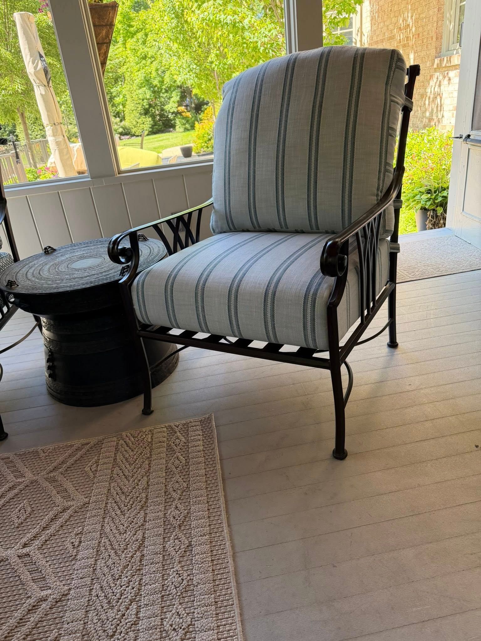 Striped upholstered chair beside a small black side table on a screened porch with trees outside