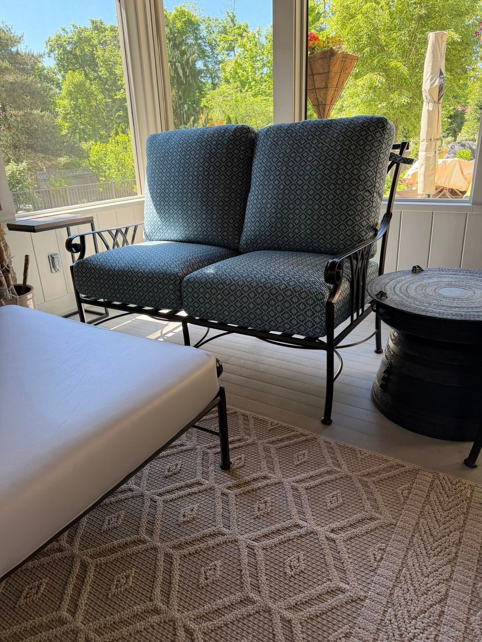 Black loveseat with blue patterned cushions beside a white chaise in a sunlit room with large windows