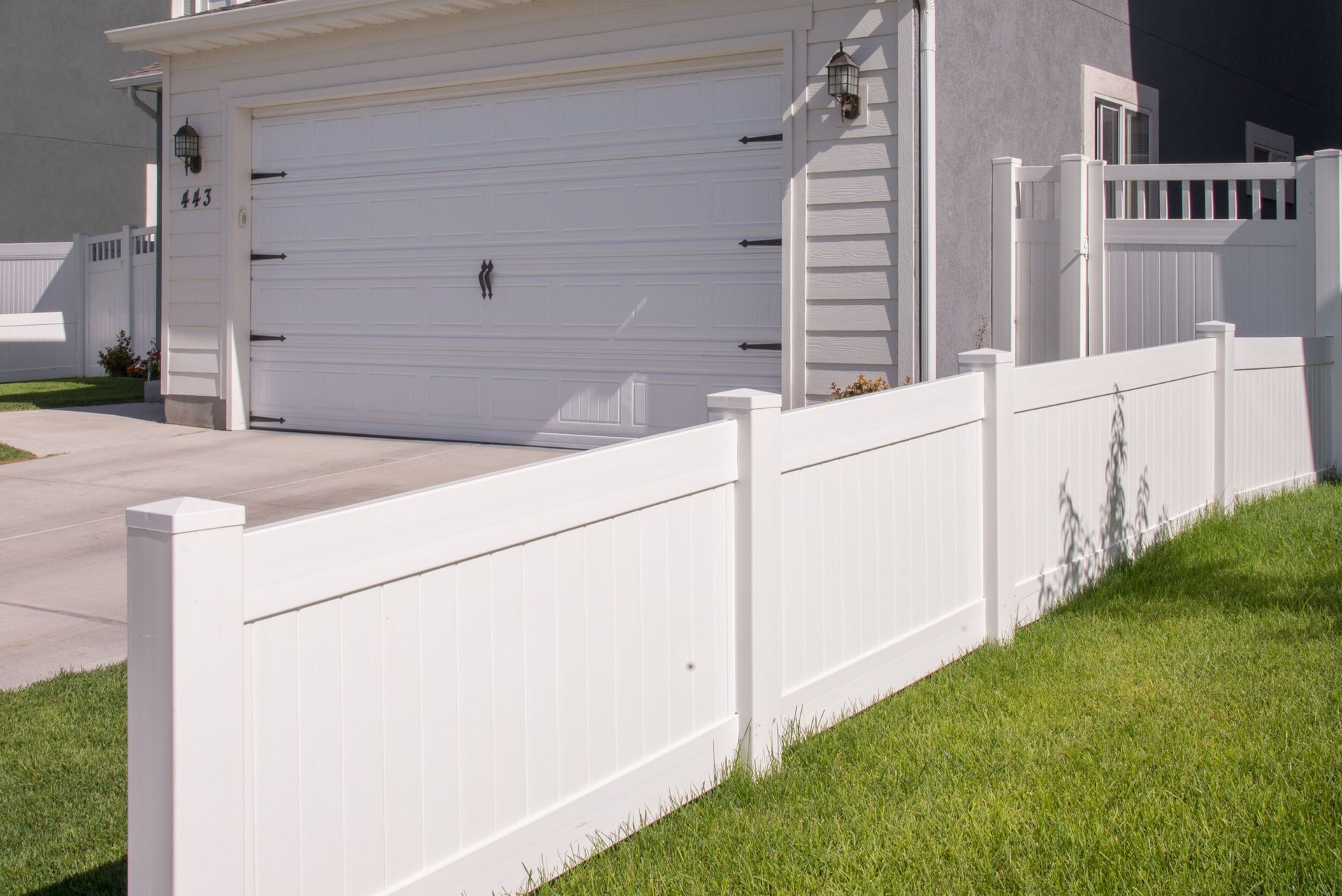 A white fence is in front of a house with a garage.
