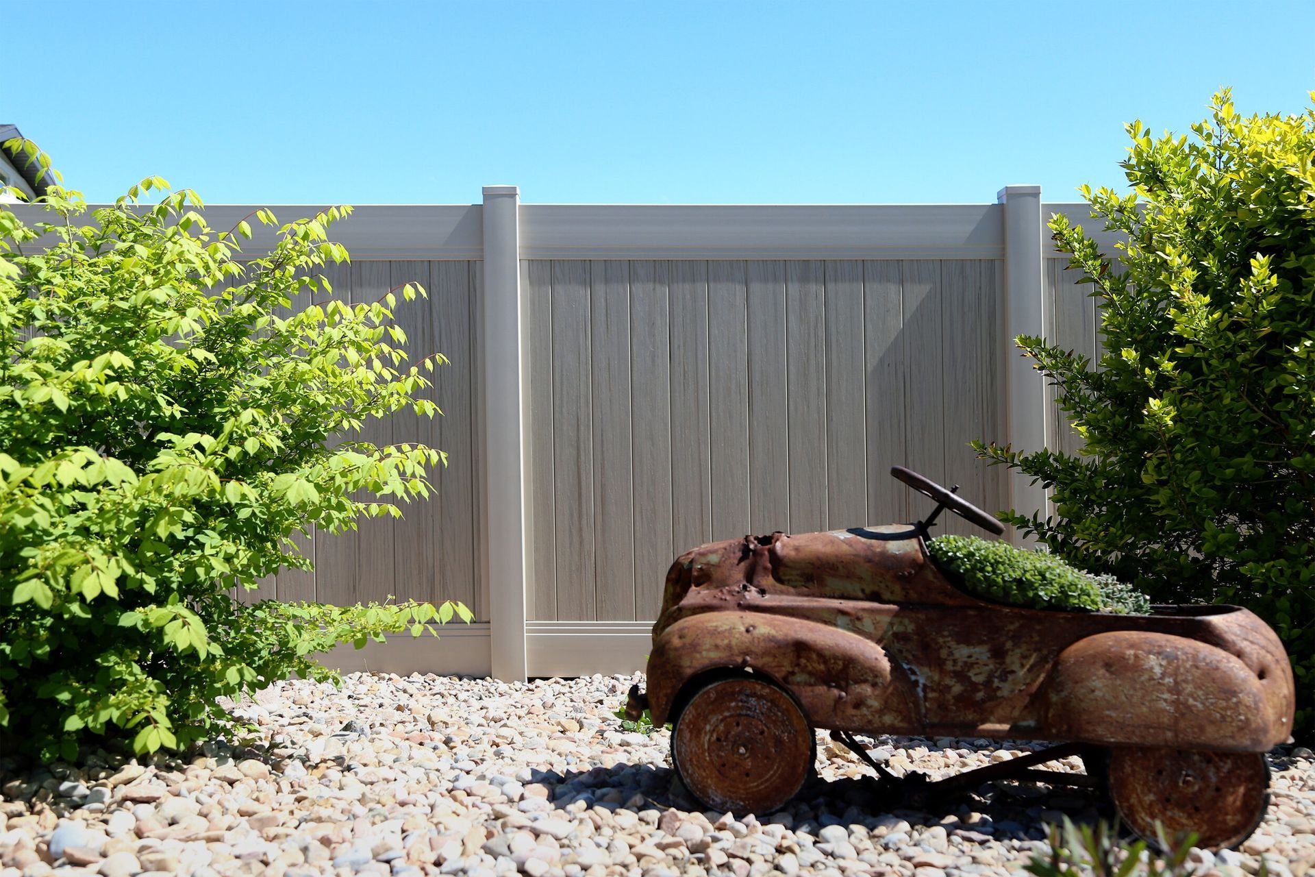 A rusty toy car is parked in front of a white fence.