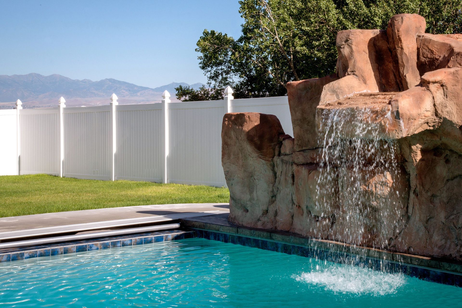 A swimming pool with a waterfall and a white fence