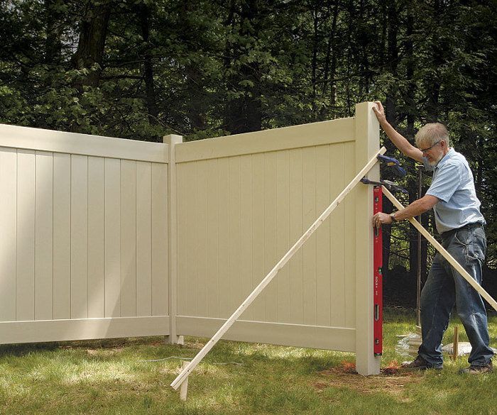 A man is measuring a fence with a red level.