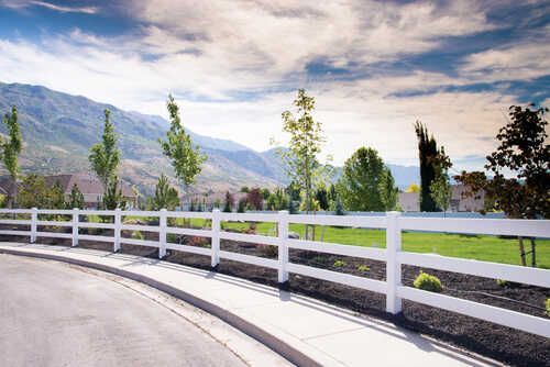 A white fence along the side of a road with mountains in the background.